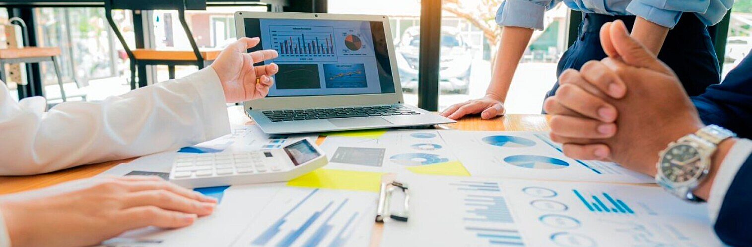 Business team analysing financial charts and graphs on a laptop and documents during a meeting.