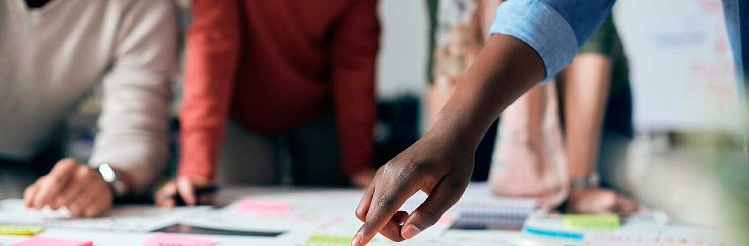 Close-up of a diverse team collaborating around a table during a planning session, pointing at documents and sticky notes.