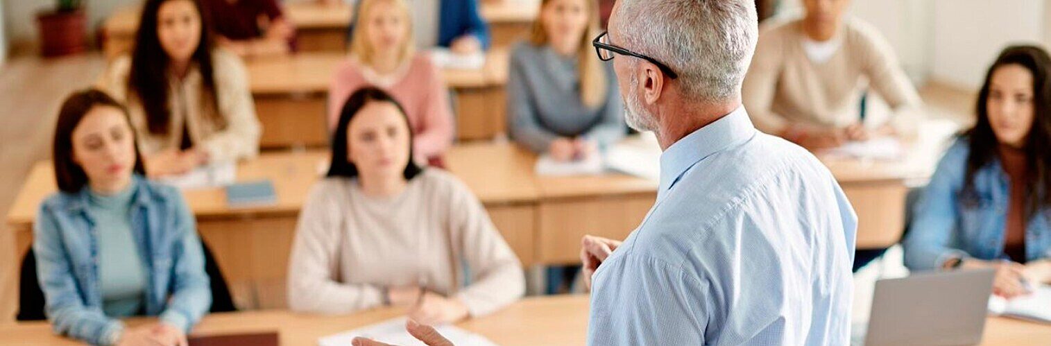 University lecturer teaching students seated at desks in a lecture theatre.