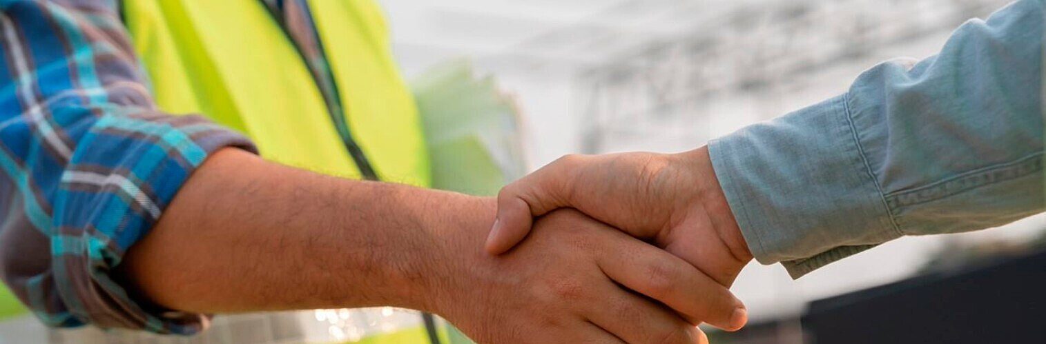 Close-up of a firm handshake between two men, one wearing a high-vis vest and checked shirt.