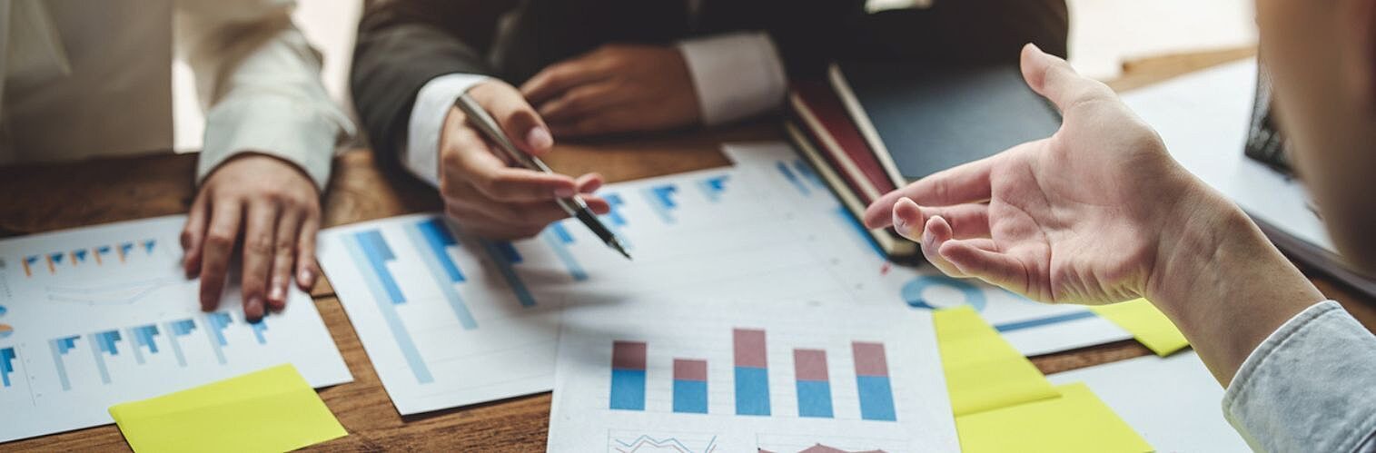 Business meeting with professionals analysing financial charts and graphs on a wooden table, discussing data insights and strategies.