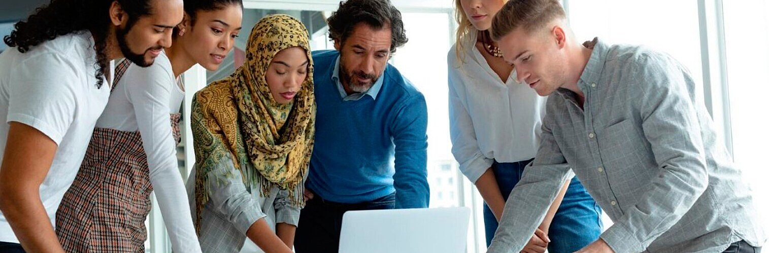 Diverse group of colleagues collaborating closely around a laptop during a team meeting in an office.