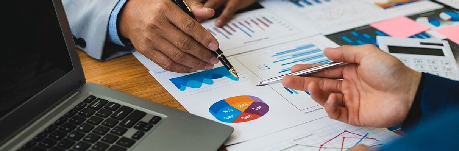 Close-up of business colleagues analysing financial data, pointing with pens at charts and graphs on documents during a meeting.