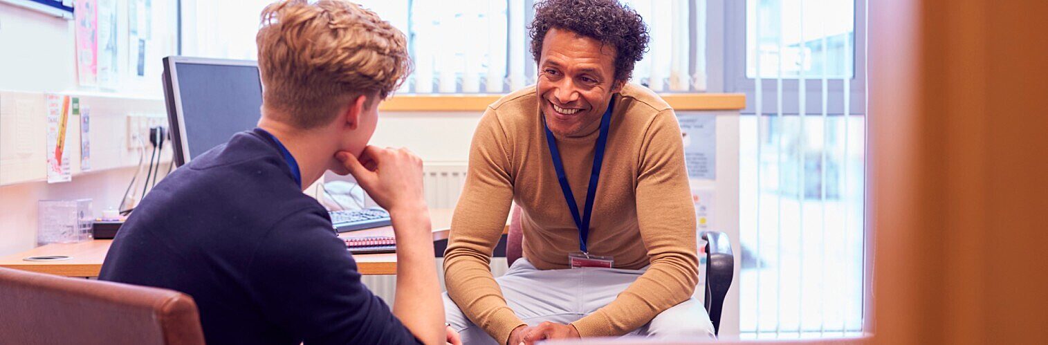 Friendly academic advisor or school counselor actively listening and speaking with a young student during a one-on-one consultation.